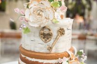 a naked and buttercream wedding cake with neutral and pastel blooms, greenery and berries, a vintage lock and a key
