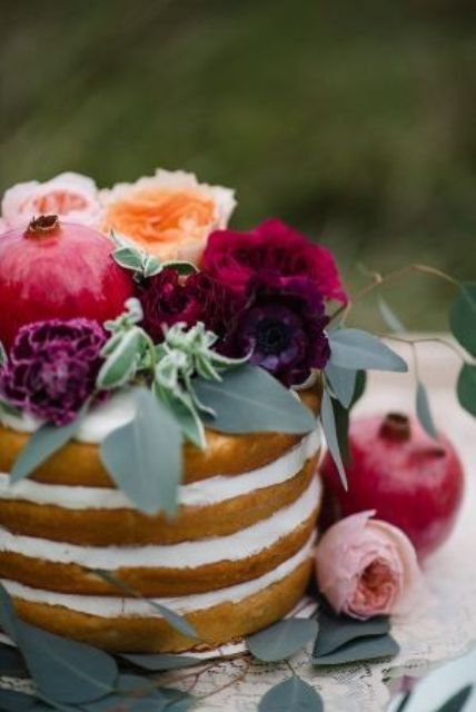 a naked wedding cake with blush, peachy, burgundy and deep purple blooms, greenery and a pomegranate is a gorgeous idea for a boho wedding