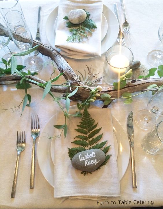a natural wedding tablescape with a branch and greenery, berries, fern leaves and pebble place cards plus candles