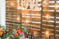 a pallet backdrop with lights and large marquee letters is a nice idea for the wedding venue backdrop
