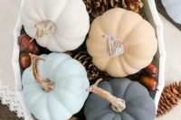 a pastel wedding centerpiece of a white bowl with pinecones, acorns, greenery and pastel pumpkins is a cool idea for the fall