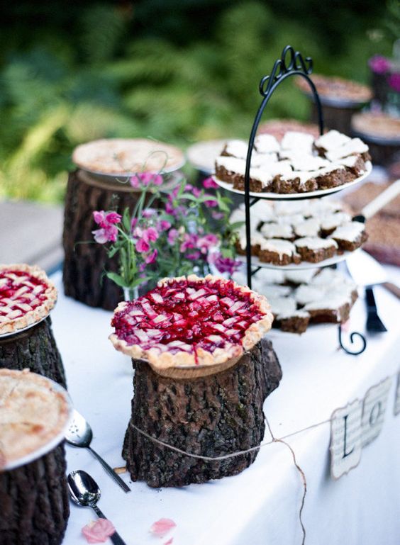 a relaxed and natural pie bar with tree stumps as pie stands, a stand with mini cakes and bright blooms in vases is great for summer