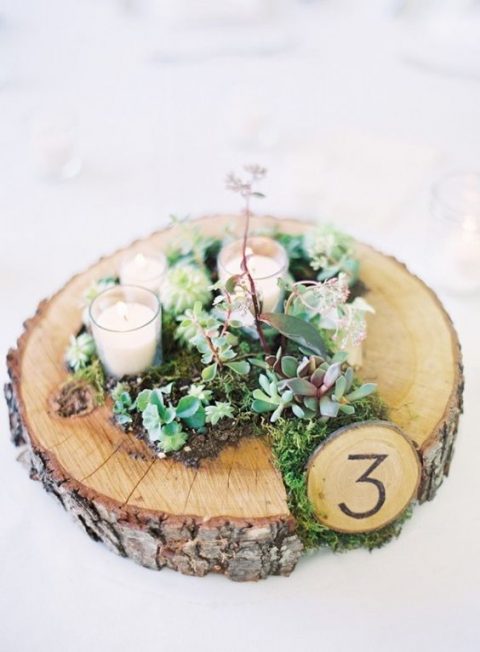 a rustic wedding centerpiece of a wood slice planter with succulents and moss, candles and a table number