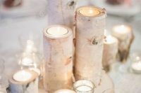 a simple and cozy winter wedding centerpiece of candles in glass and branch candleholders on a wood slice