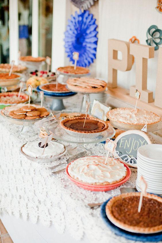 a simple and cute pie bar with a doily tablecloth, letters, paper fans and lots of pies and cookies with tags
