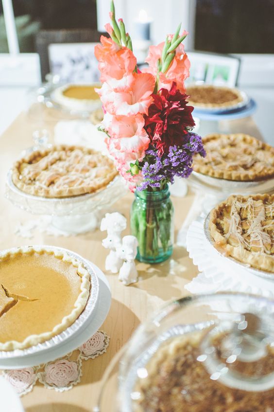 a simple and relaxed pie bar with doilies, bright blooms in a jar and white stands with pies is a very cool idea