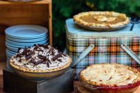a simple and rustic pie bar with crates, boxes and plaid lunch boxes is ideal for a camp wedding or a woodland one