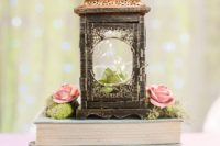 a stack of books, moss, pink roses and a large vintage lantern with a succulent inside looks rustic and vintage at the same time