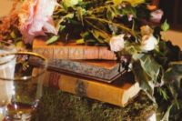 a stack of books, one of them covered with moss and with lots of lush blooms on top