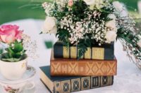 a stack of books plus a lush floral arrangement on top is a beautiful garden wedding centerpiece idea