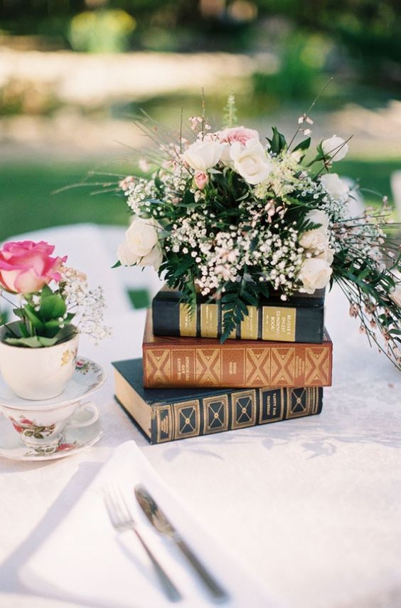 a stack of books plus a lush floral arrangement on top is a beautiful garden wedding centerpiece idea