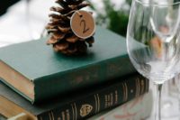 a stack of vintage books, a pinecone with a table number tag for a winter wedding centerpiece