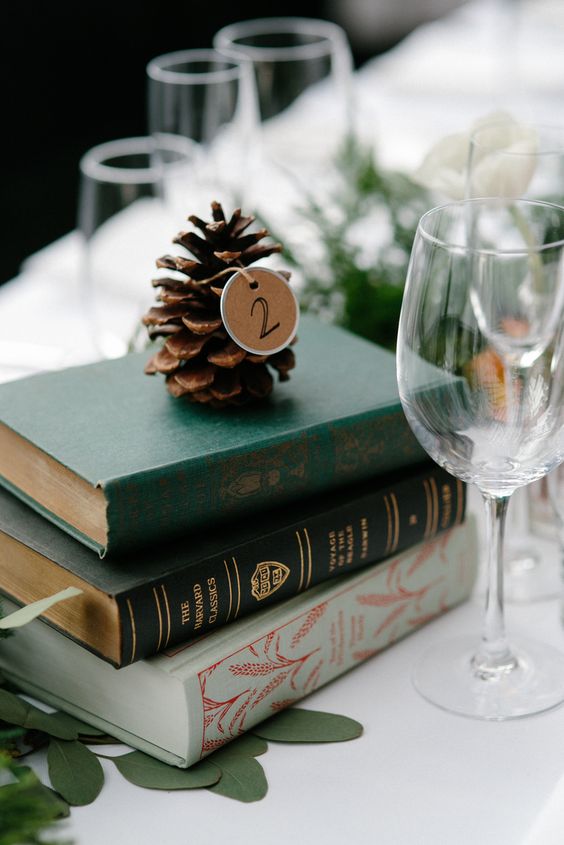 a stack of vintage books, a pinecone with a table number tag for a winter wedding centerpiece