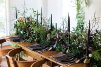 a statement wedding tablescape with black candles, greenery and dark blooms plus matte black plates for a forest-inspired wedding