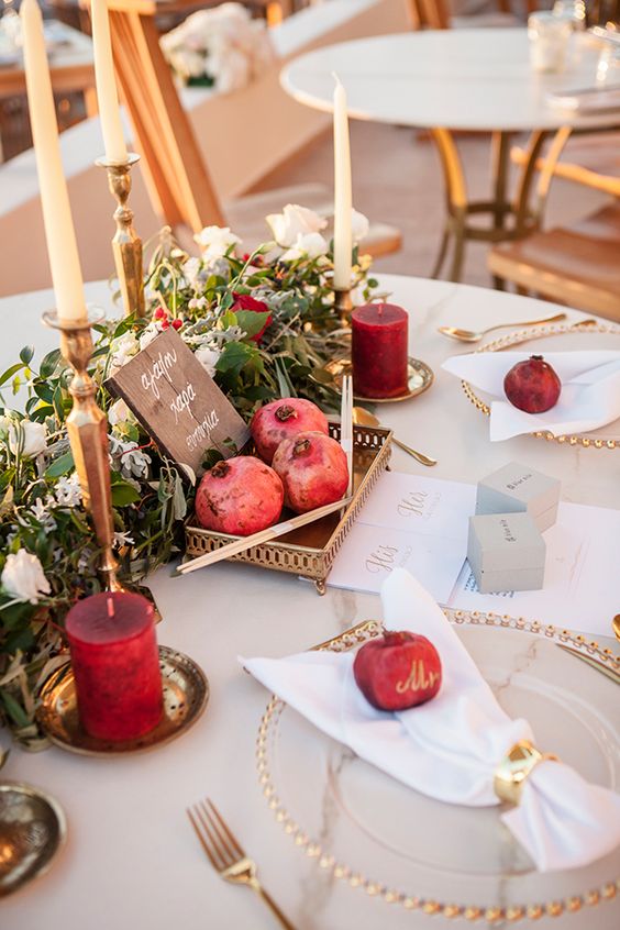 a super bold wedding tablescape with a greenery, white and burgundy bloom runner, neutral and burgundy candles, pomegranates in a tray and on the table