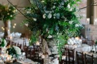 a super lush and oversized wedding centerpiece of a tree stump with lots of textural greenery, some white blooms and branches plus candles around