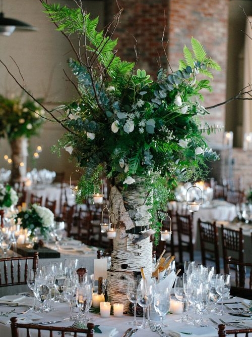 a super lush and oversized wedding centerpiece of a tree stump with lots of textural greenery, some white blooms and branches plus candles around