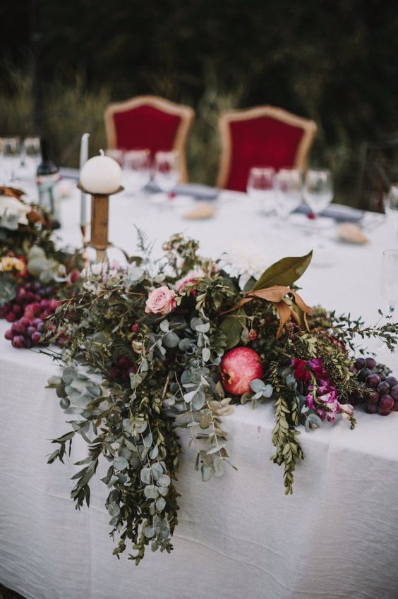 a super lush fall wedding centerpiece of greenery, foliage and pink and fuchsia blooms plus pomegranates is amazing for the fall