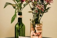 a vineyard wedding centerpiece of wine corks with a table number, bright blooms and greenery in a bottle and vase with corks