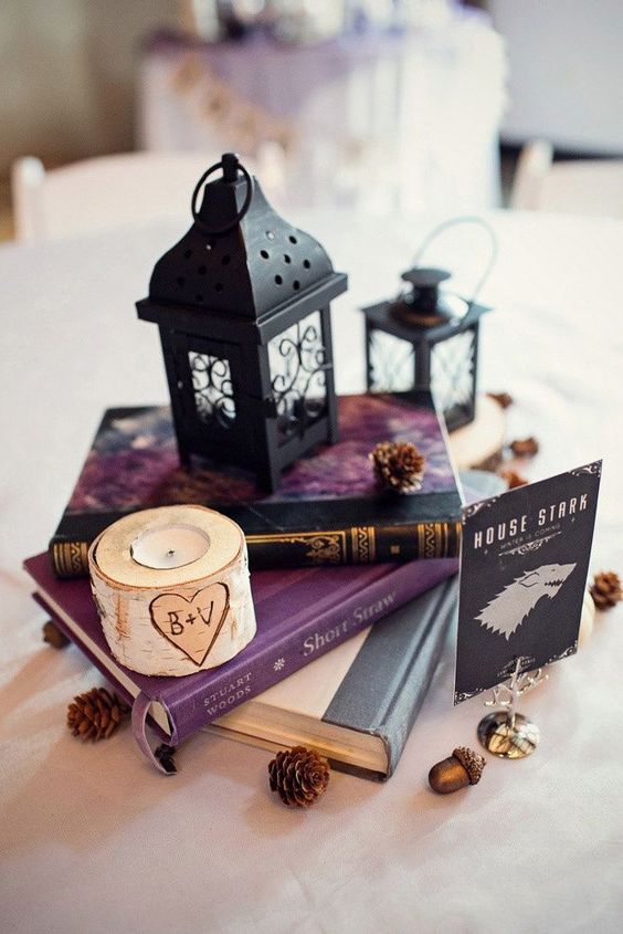 a vintage book centerpiece with small black lanterns, pinecones and a birch candle holder
