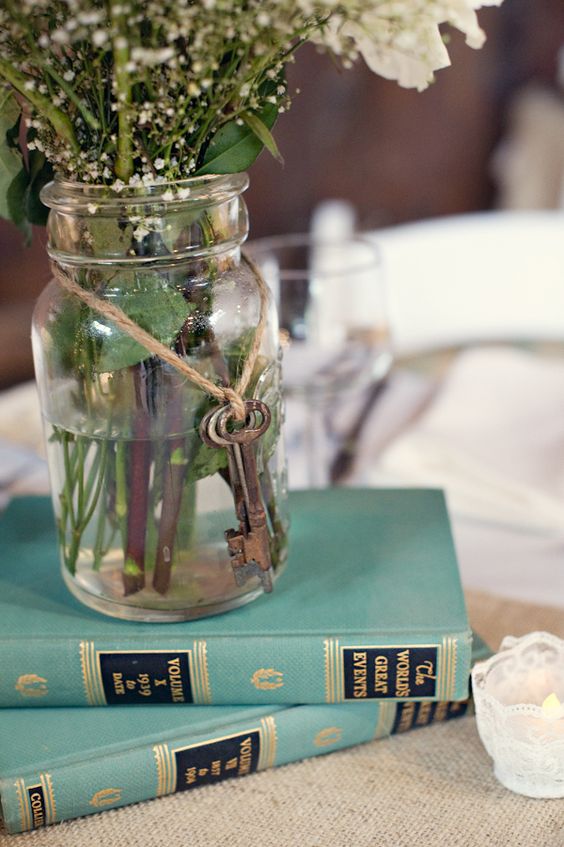 a vintage rustic wedding centerpiece of a stack of books, a jar with vintage keys and some white blooms is very easy to DIY