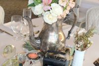 a vintage wedding centerpiece including vintage books, a camera, blush and white blooms in vases and an old teapot plus doilies is a cool idea