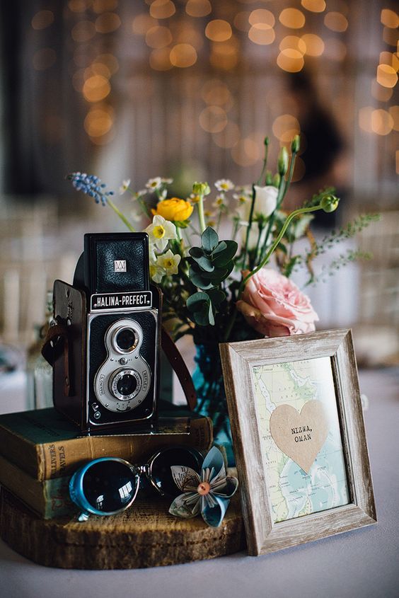 a vintage wedding centerpiece of a wood slice, vintage books, a vintage camera, pretty blooms and a small amp decoration