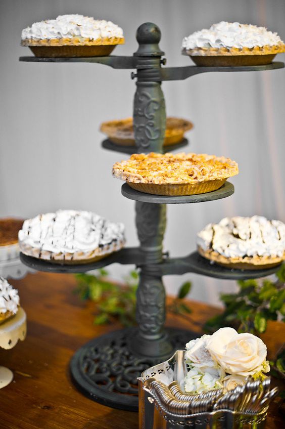 a vintage wedding pie bar with a metal stand and lots of pies, some neutral blooms and greenery is very elegant