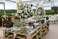 a wedding dessert table made of pallets with blooms and with a glass tabletop is a fun and cute idea with a rustic feel
