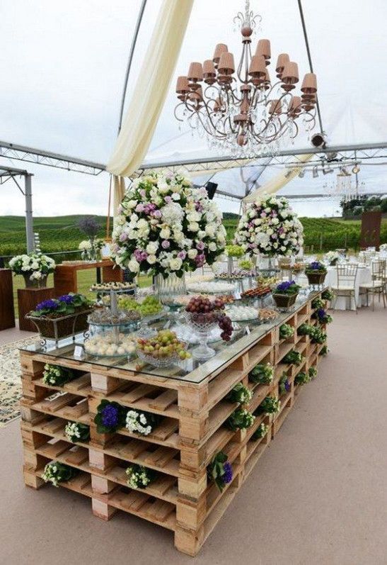 a wedding dessert table made of pallets with blooms and with a glass tabletop is a fun and cute idea with a rustic feel