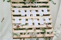 a wedding seating chart with a pallet on stands and monograms and much greenery