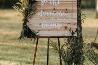 a wedding sign decorated with various greenery arrangements and a vintage candle lantern is a lovely rustic decor idea
