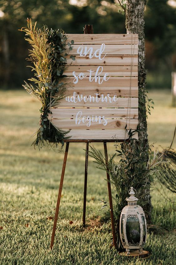 a wedding sign decorated with various greenery arrangements and a vintage candle lantern is a lovely rustic decor idea