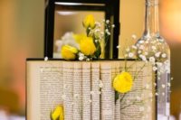 a whimsy centerpiece of a bottle, a lantern, an open book wth yellow roses and babys breath tucked in between pages