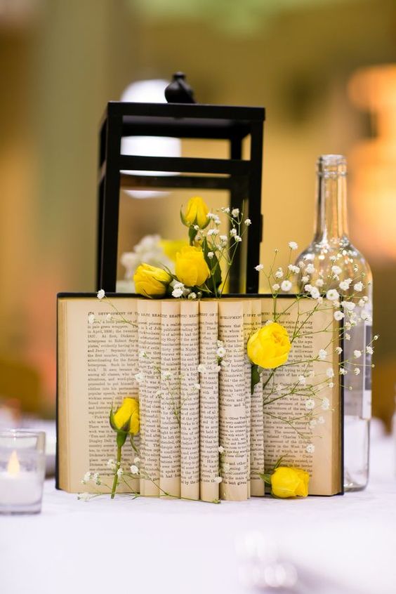 a whimsy centerpiece of a bottle, a lantern, an open book wth yellow roses and babys breath tucked in between pages