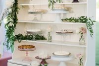 a white buffet with greenery and white blooms, blush blooms in jars and various stands with pies is amazing for a wedding