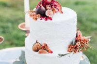 a white buttercream wedding cake decorated with pink blooms, greenery, figs and pomegranates is a gorgeous idea for the fall