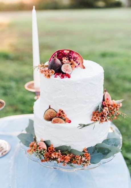 a white buttercream wedding cake decorated with pink blooms, greenery, figs and pomegranates is a gorgeous idea for the fall
