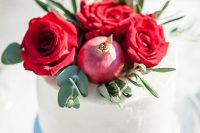 a white buttercream wedding cake with red roses, pomegranates and greenery is a fantastic idea for a fall wedding
