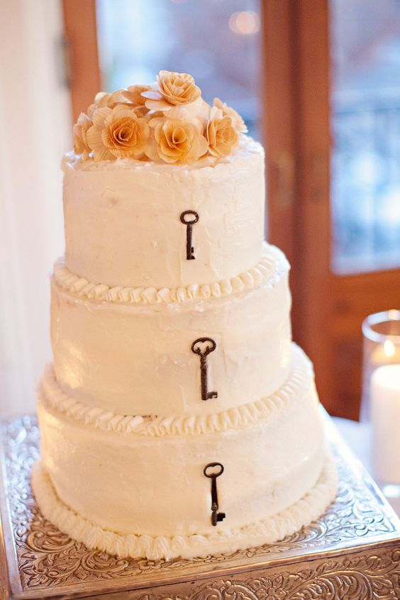 a white buttercream wedding cake with vintage keys and peachy blooms is a lovely idea for a rustic or vintage wedding