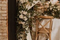 a white curtain decorated with lush greenery and white blooms is beautiful wedding decor with a strong natural feel