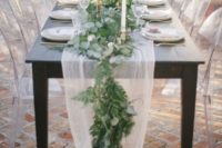 a white tulle and greenery table runner with candles in elegant metallic candle holders for a fresh look
