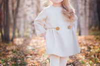 a white warm mini dress with long sleeves and buttons, white tights and geometric shoes for a modern winter flower girl