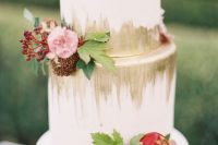 a white wedding cake with gold decor, pink blooms, greenery, berries and tiny pomegranates is an elegant idea for a fall wedding