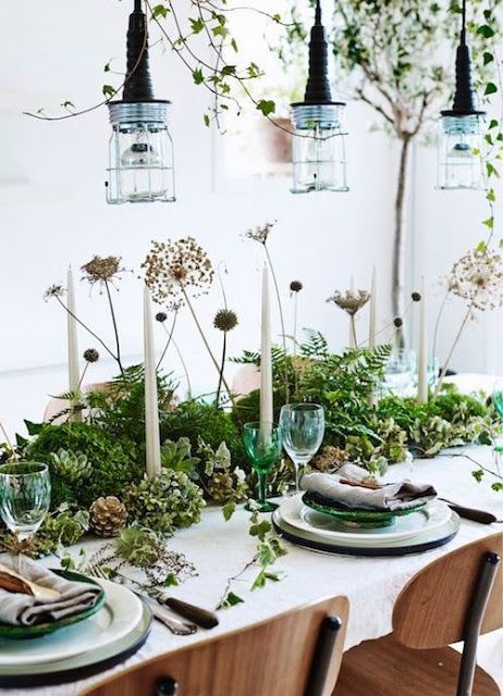 a woodland wedding tablescape with lush greenery, succulents, dried plants, white candles, green and neutral plates