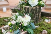 an all-natural wedding centerpiece of moss, pebbles, a wood slice and a tree stump, some neutral blooms and berries