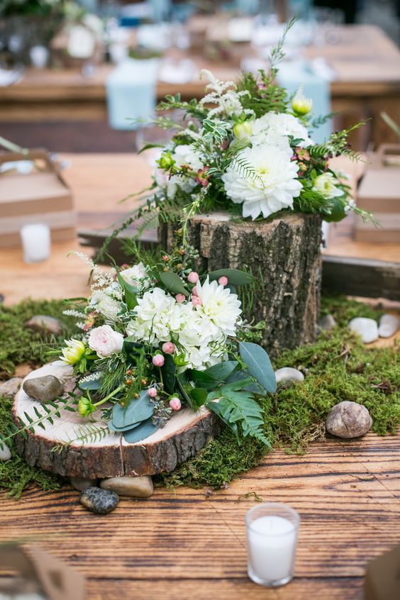 an all-natural wedding centerpiece of moss, pebbles, a wood slice and a tree stump, some neutral blooms and berries