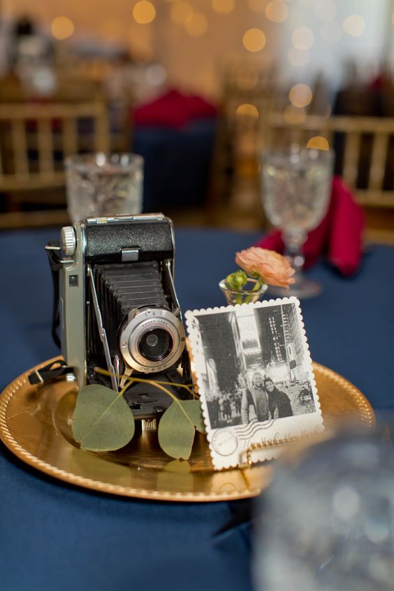 an elegant vintage wedding centerpiece of a gold dish, greenery, a vintage camera and a photo, a single bloom in a vase