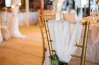 an elegant wedding chair cover idea – gold chairs draped in white tulle and greenery