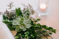 an opened book with lush greenery, blooms and a large succulent is a chic and refreshing centerpiece idea